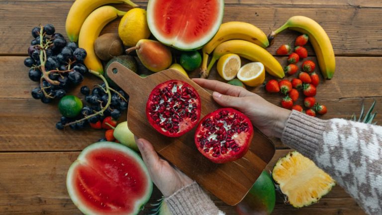 Vibrant fruits including pomegranates, bananas, and watermelon on a rustic wooden table.