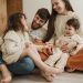 Smiling family of four sitting on the living room floor, enjoying quality time together.
